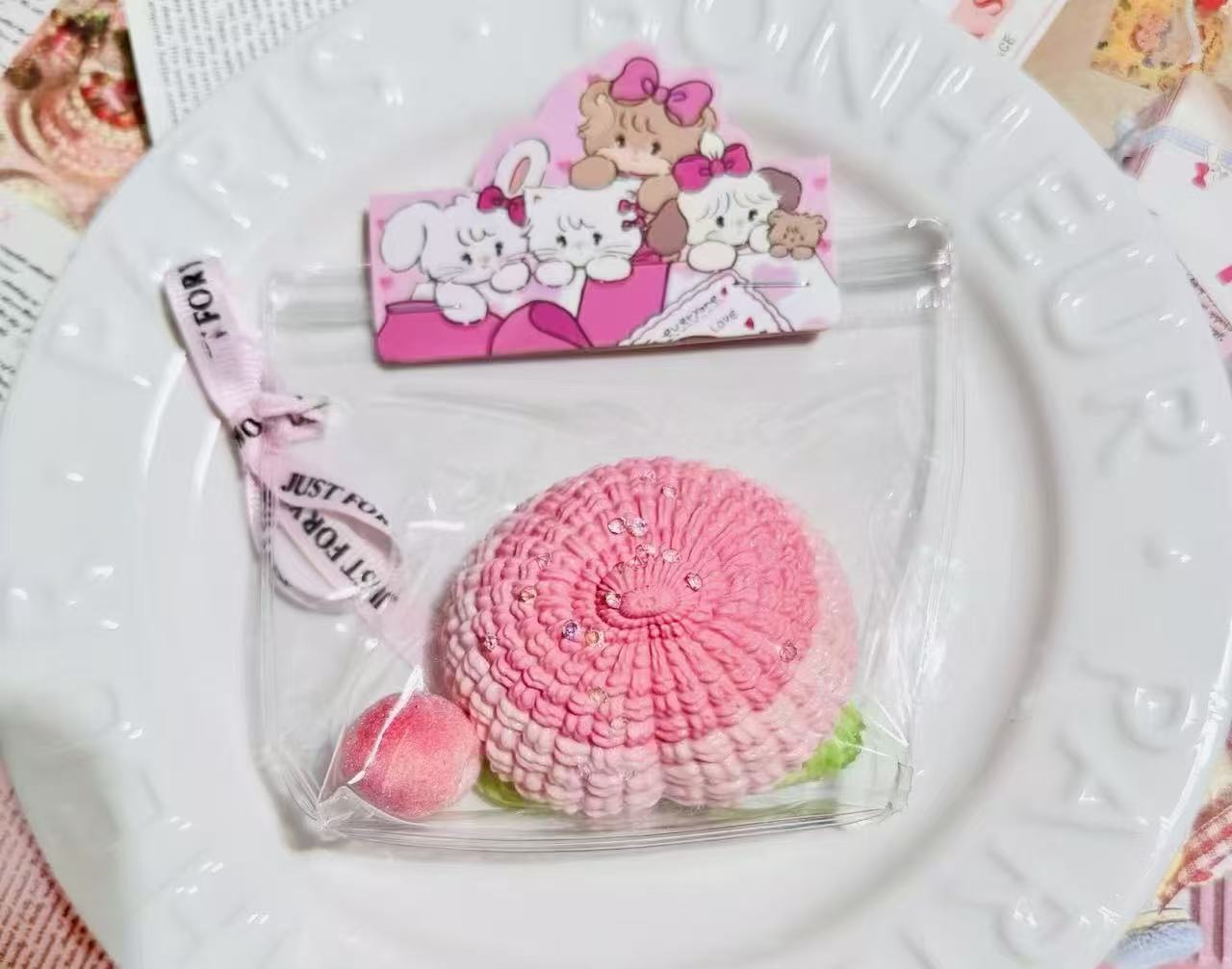 A handmade peach crochet squishy with pink textured details, sparkly beads, and a mini peach charm, packaged in a clear bag with ribbon.