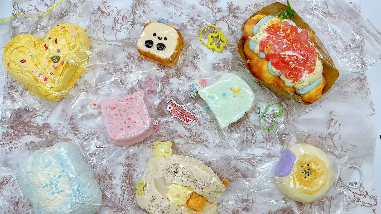 Variety of Pawkemon blind bag squishies laid out, including toast, decorated cream buns, pastel-colored bread slices, and textured clouds, all individually packaged with cute charms.