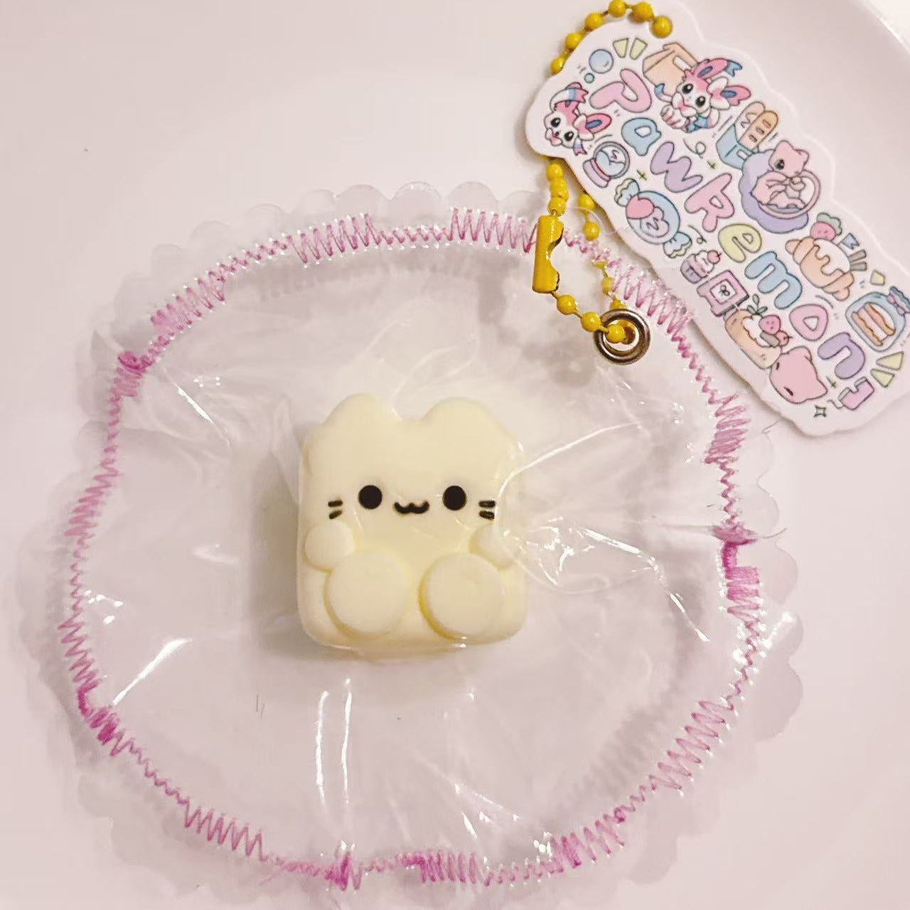 Custard Cube Cat Taba Squishy displayed on a plate with delicate frilled wrapping and Pawkemon tag, featuring a mini 15g cube cat with short limbs.