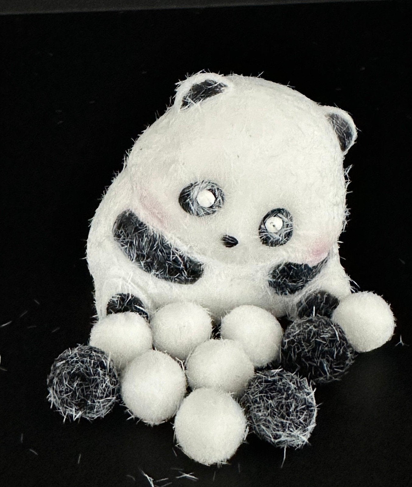 Close-up of flocked cute panda squishy on black background, showing soft velvet-like surface and chubby panda pose for stress relief.