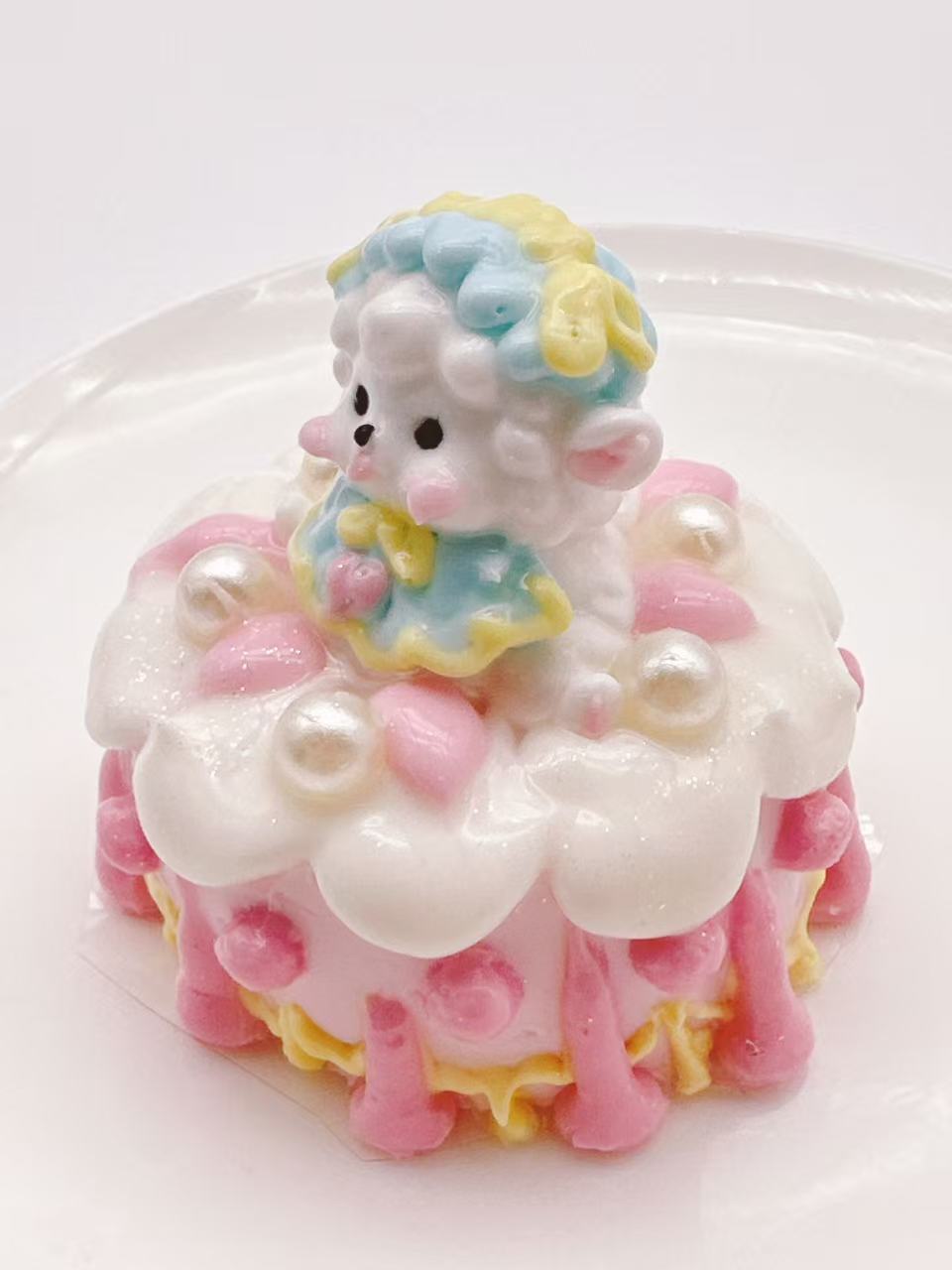 Side view of a handmade Lamb Pearl Cake Taba Squishy showing the pastel cake layers, pink frosting, pearl-like decorations, and lamb figure