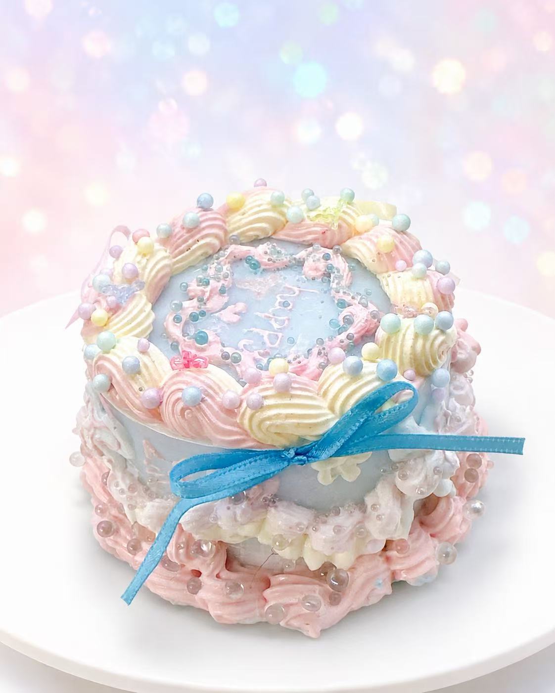 Side view of Ocean Cake Taba Squishy showing layered pastel cake details, blue ribbon bow, pearl decorations, pink cream piping, and handmade silicone texture.