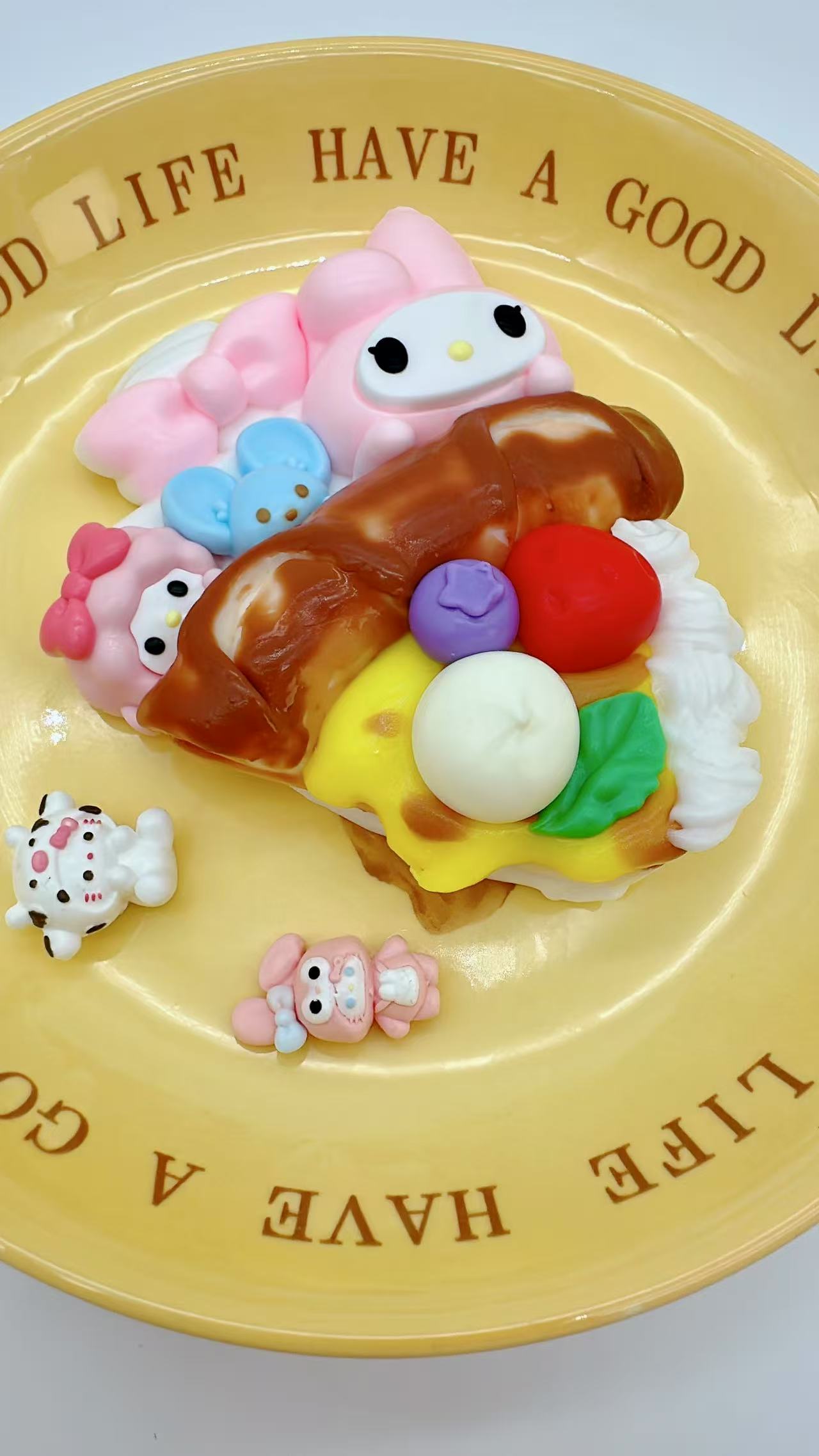 Top-down view of Sanrio Pizza Taba Squishy with My Melody, Kuromi, and Cinnamoroll surrounded by whipped cream, berries, and cheese on a pizza base.