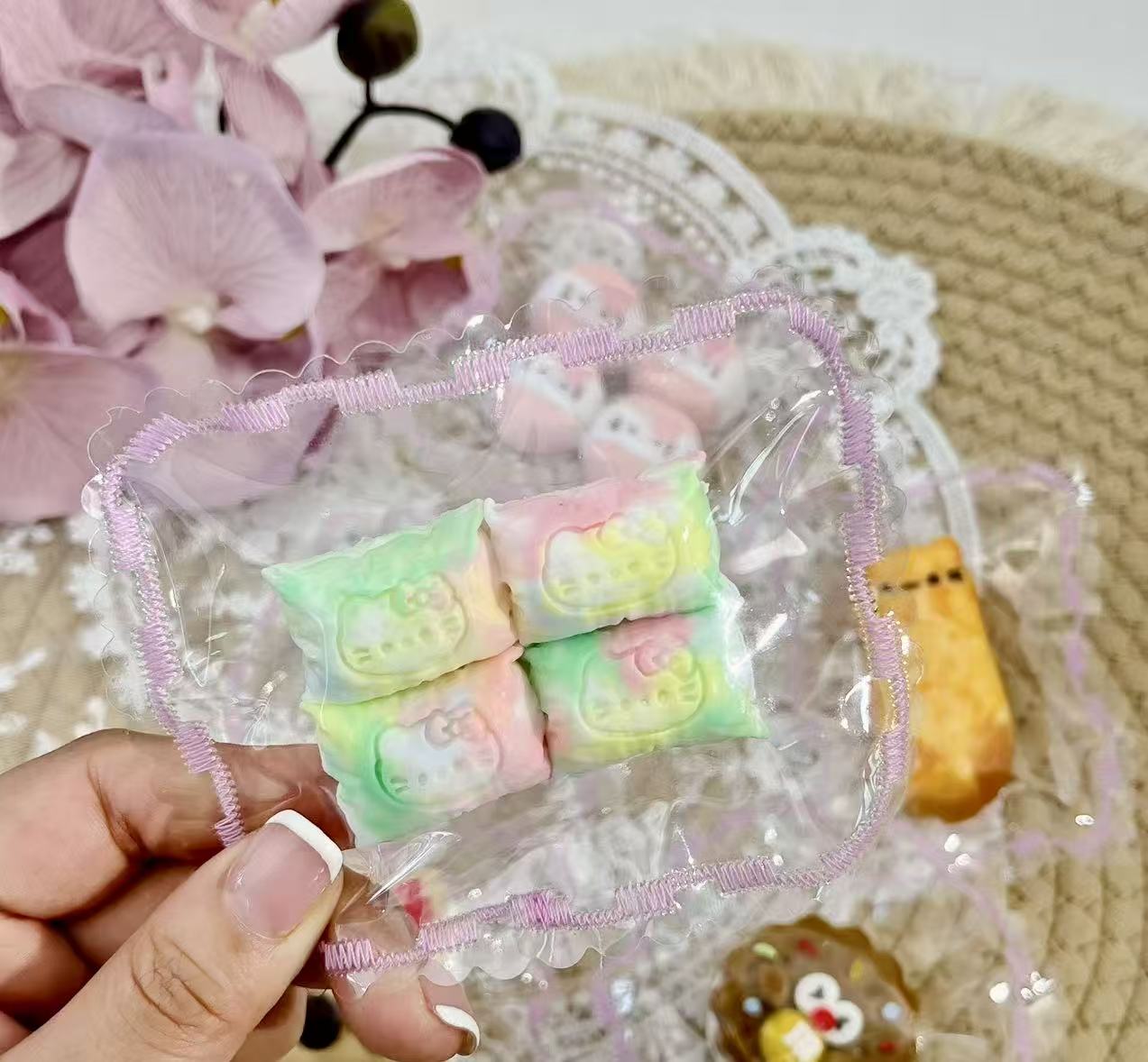Four pastel rainbow pillow-shaped Hello Kitty squishies inside a lace-trimmed transparent bag