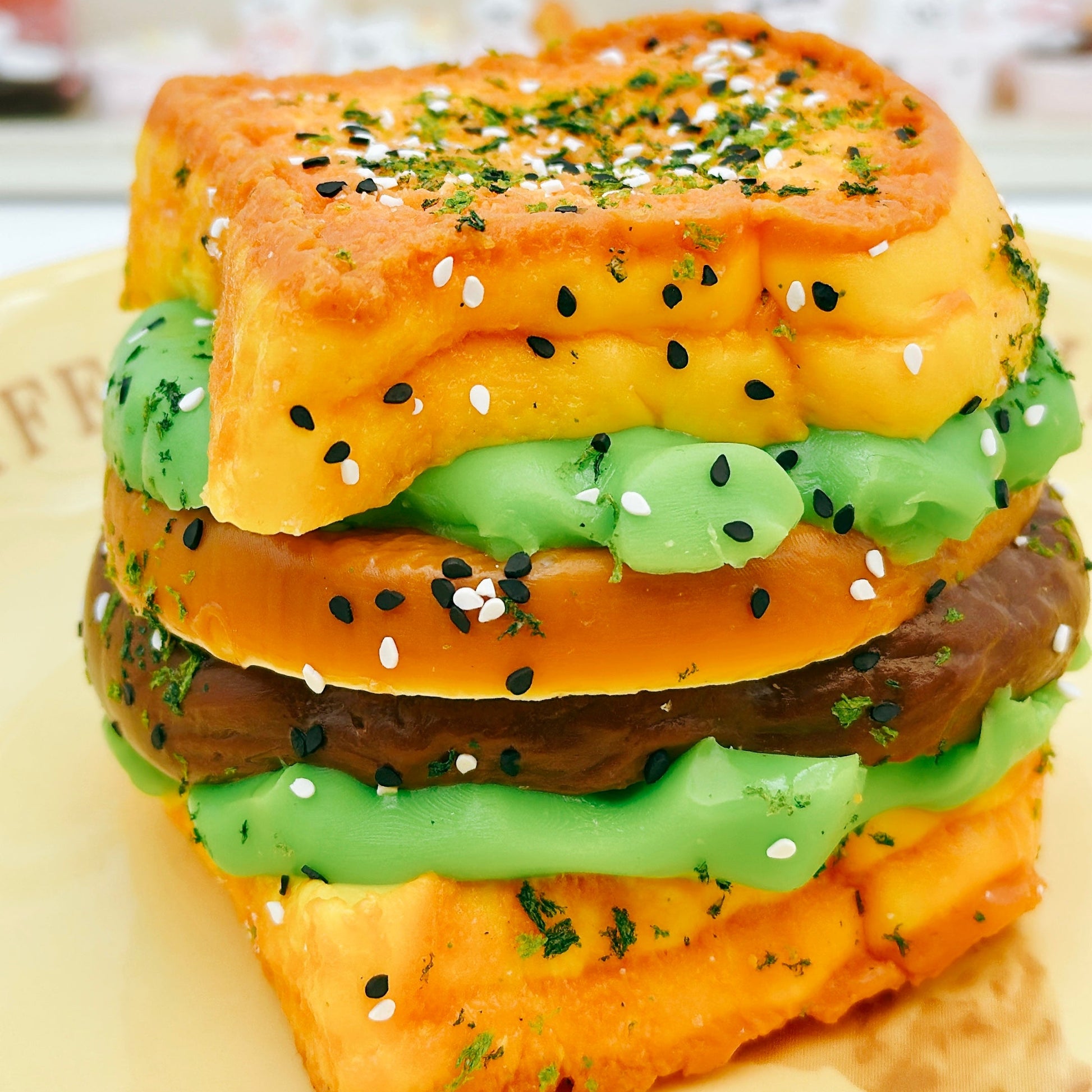 Side view of the handmade 6-Layer Burger Taba Squishy with vibrant green and brown fillings, toasted bun texture, and sesame details.