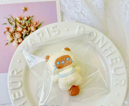 A handmade Siamese cat squishy with creamy fur, brown accents, and blue dotted eyes, packaged in a clear bag with ribbon.