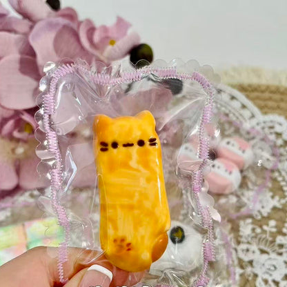 A golden-yellow kitty-shaped squishy resembling a cheese bar, packaged in a lace-trimmed transparent pouch.