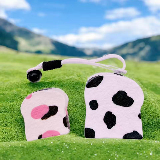 Thick Cow Toast and Pink Cow Toast Taba Squishy displayed outdoors on grass with mountain background – kawaii handmade squishy toys perfect for collectors and stress relief.
