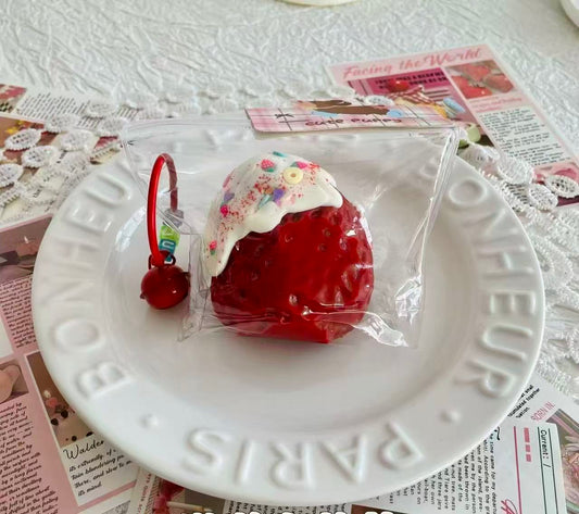 A jumbo strawberry squishy topped with creamy drizzle, glitter, and sprinkles, packaged in a transparent bag