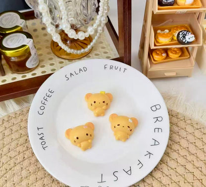 Three golden-yellow handmade bear squishies with tiny floral details, displayed on a white plate 