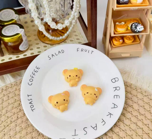 Three golden-yellow handmade bear squishies with tiny floral details, displayed on a white plate 