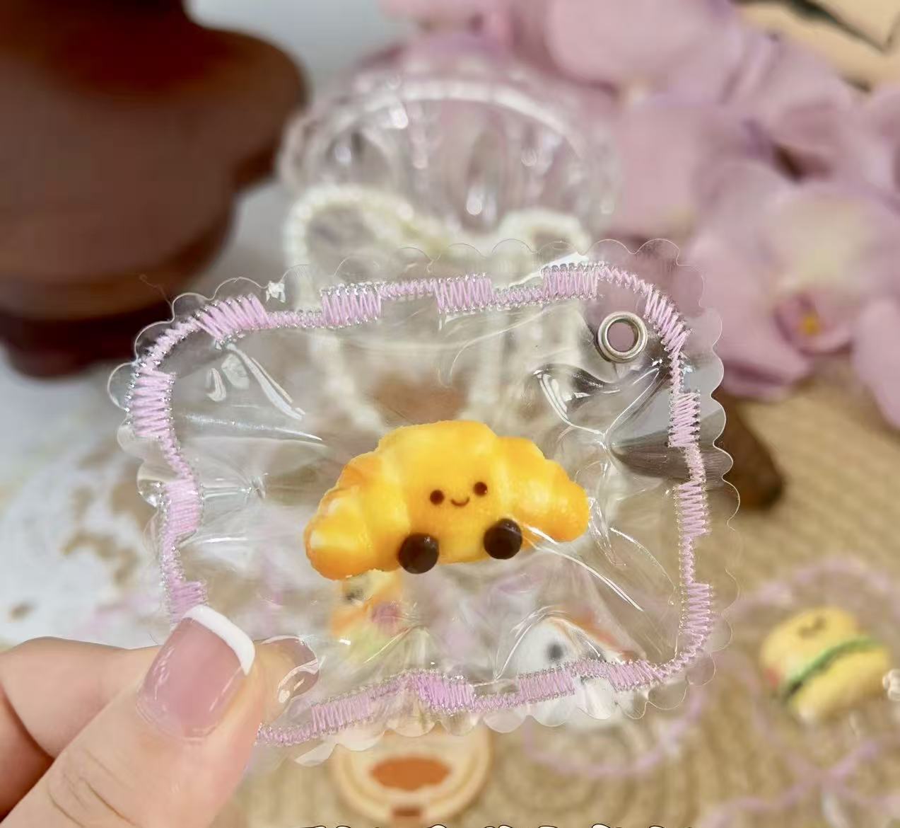 A cute croissant-shaped squishy toy with a smiling face, bright golden color, packaged in a transparent pouch with machine-stitched decorative edges.