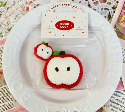 A pair of handmade apple squishies with a knitted texture design, one large and one mini, packaged in a clear bag with a “Good Luck” header card.