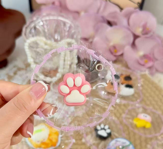 A mini pink paw squishy with white paw pads, packaged in a transparent pouch with pink decorative stitched edges.