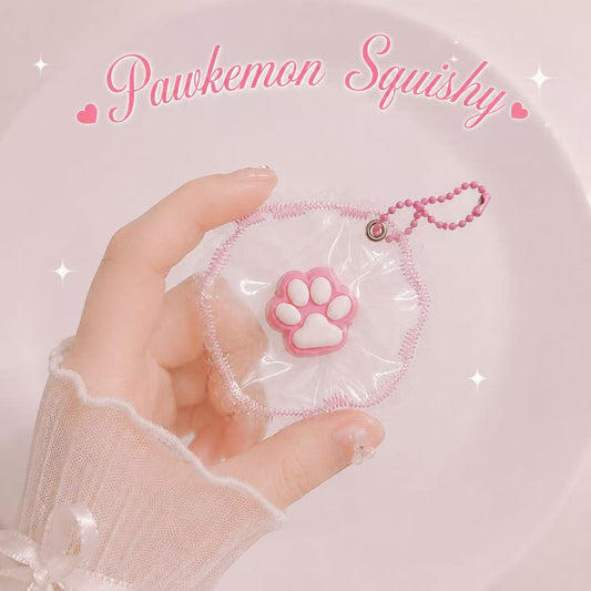 A hand  holds a pink and white Pawkemon squishy toy. The squishy features a clear plastic pouch with a pink stitched border and a central pink paw print silicone squishy.