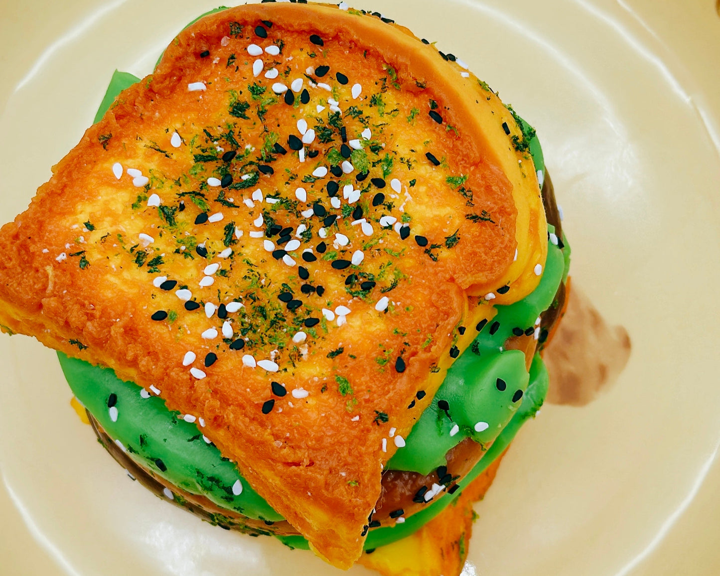 Top view of the 6-Layer Burger Taba Squishy featuring stacked buns, patty layers, and sesame seed topping on a beige plate.