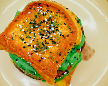 Top view of the 6-Layer Burger Taba Squishy featuring stacked buns, patty layers, and sesame seed topping on a beige plate.