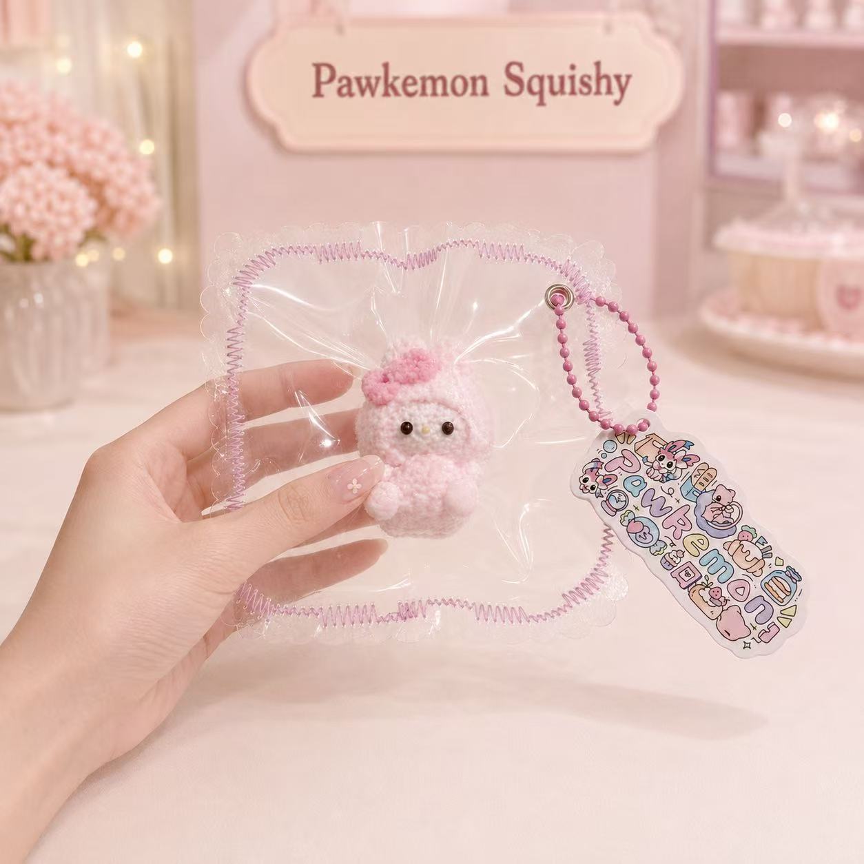 Hand holding the packaged Pink Bunny Taba Squishy, showing its soft textured bunny design, pink bead chain, colorful tag, and handmade Pawkemon Squishy packaging.