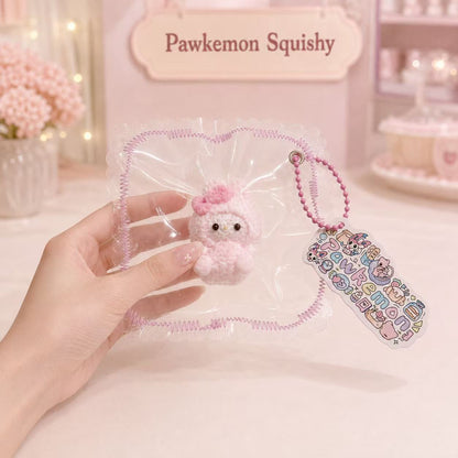 Hand holding the packaged Pink Bunny Taba Squishy, showing its soft textured bunny design, pink bead chain, colorful tag, and handmade Pawkemon Squishy packaging.