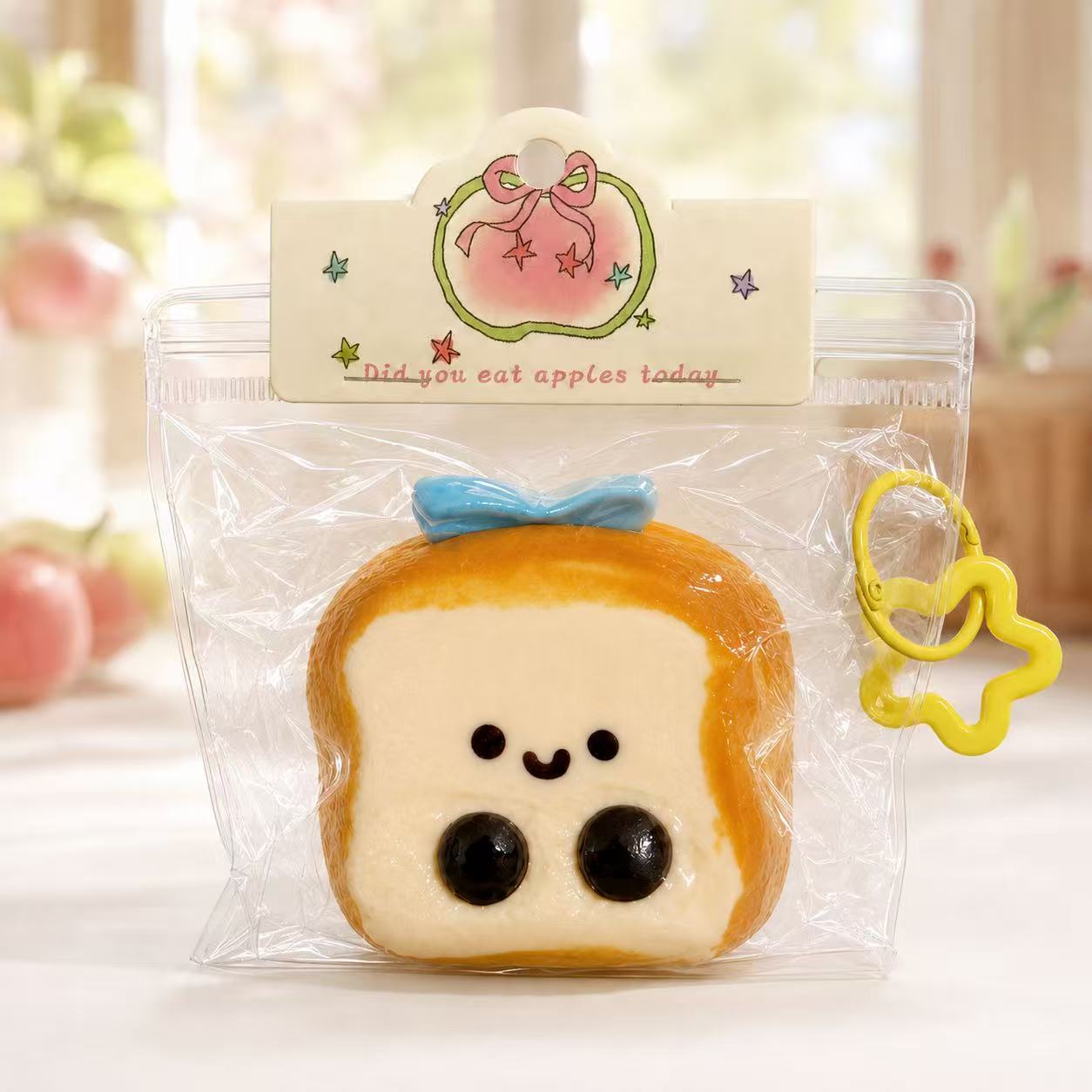 Baby Toast Taba Squishy by Pawkemon Squishy, a handmade silicone toast squishy with soft bread texture, cute baby face design, clear packaging, blue bow, and yellow charm.