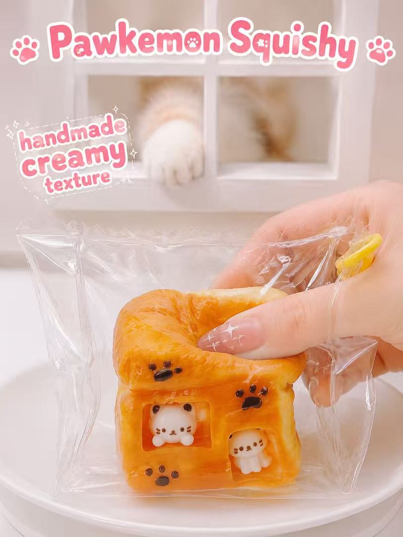 Hand squeezing Cat Toast House Taba Squishy by Pawkemon Squishy, showing the soft creamy texture, cat window details, and handmade toast design.