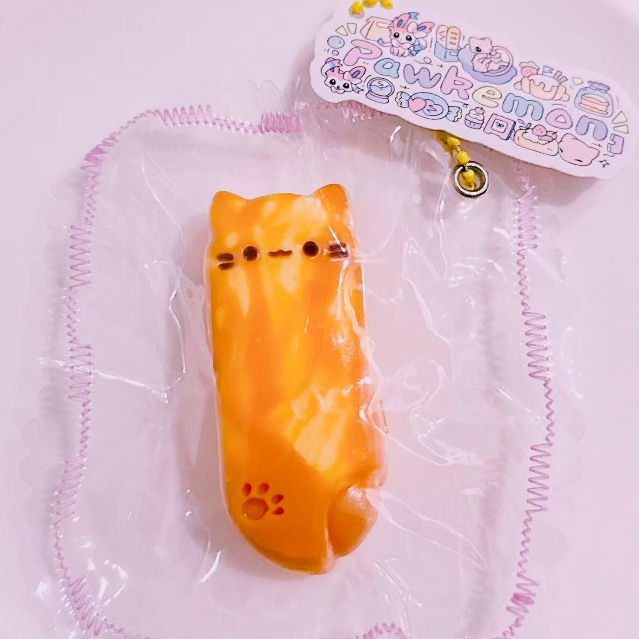Cheese Melt Kitty Bar Taba Squishy featuring a cute melted cheese cat design with tiny paw print detail, wrapped in frilled clear packaging. Handmade silicone squishy by Pawkemon.
