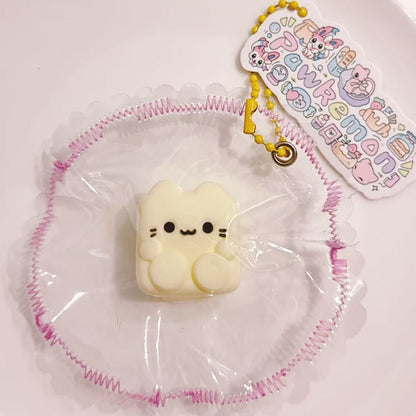 Custard Cube Cat Taba Squishy displayed on a plate with delicate frilled wrapping and Pawkemon tag, featuring a mini 15g cube cat with short limbs.
