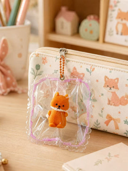 Orange Fox Taba Squishy hanging from a pastel children’s pencil pouch as a bag charm, with transparent PVC packaging, pink stitching, and orange bead chain.