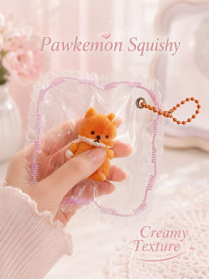 A delicate feminine hand gently squeezing the Fox Taba Squishy through its fully transparent PVC pouch, showing its soft creamy texture and handmade details.
