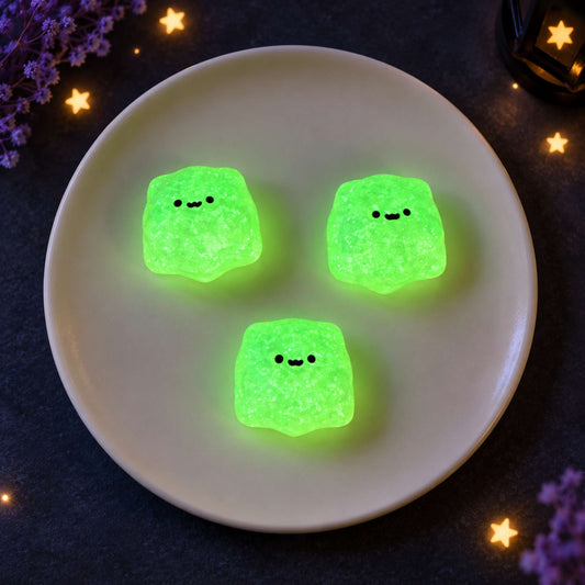 Three handmade mini ghost Taba Squishies glowing bright green on a white plate in a dark starry setting.