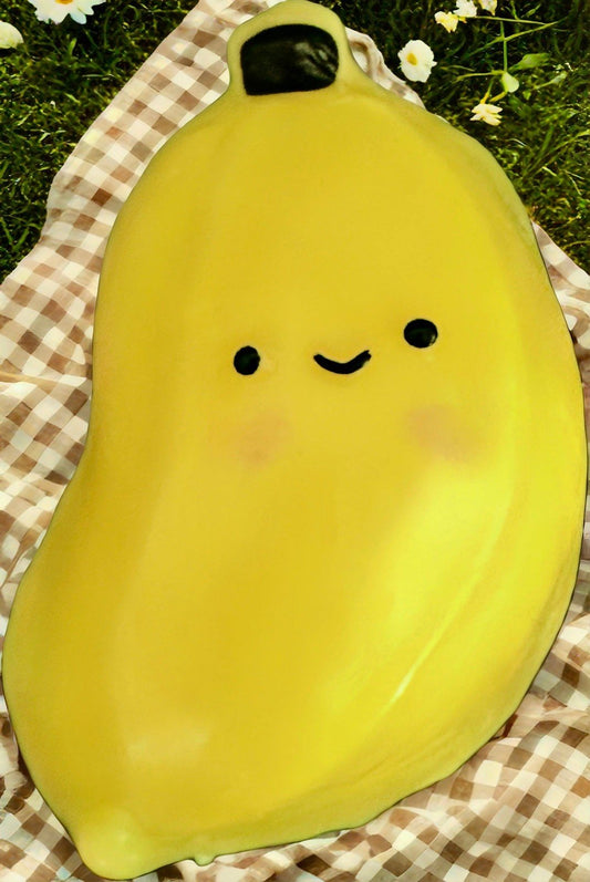 Adorable kawaii banana squishy displayed on a picnic mat, featuring bright yellow color, smiling face, and soft slow rise texture.