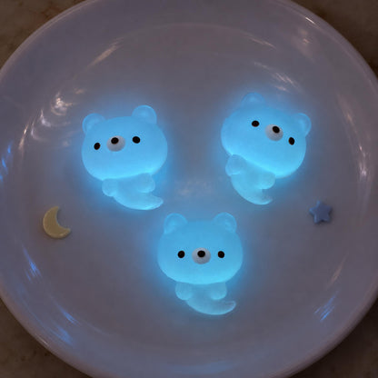 Three mini ghost bear Taba Squishies glowing blue on a dark plate with small moon and star accents.