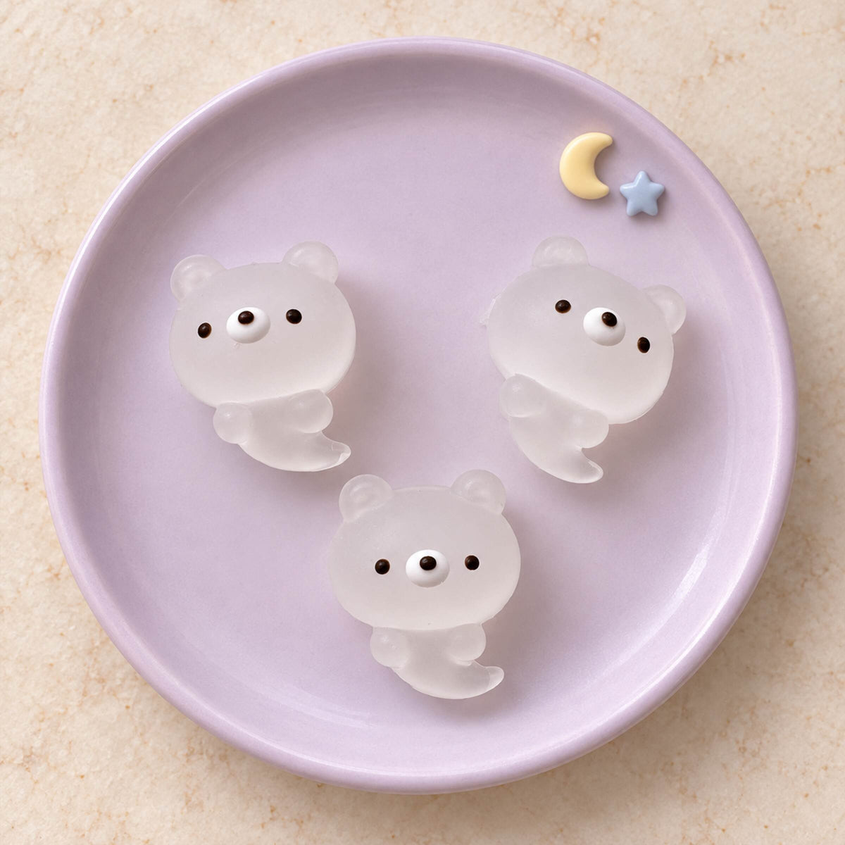 Three translucent white mini ghost bear Taba Squishies on a lavender plate with yellow moon and blue star decorations.
