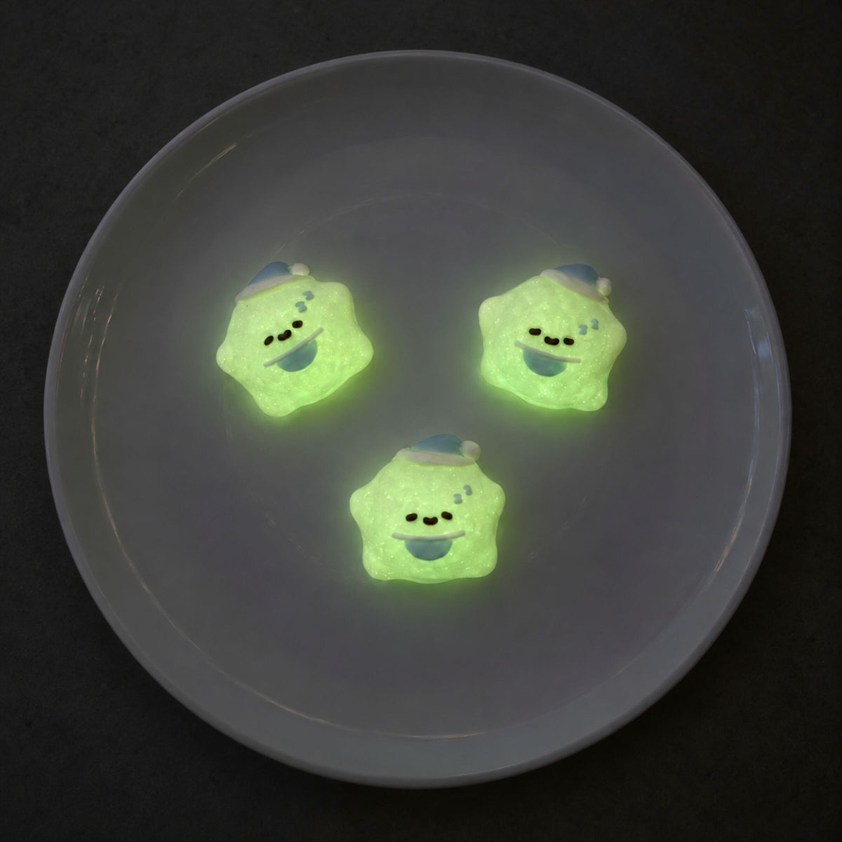 Three mini star Taba Squishies glowing soft green on a dark gray plate in a triangular arrangement.