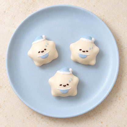 Three cream mini star Taba Squishies with blue nightcaps, crescent moons and cute faces on a light blue plate.