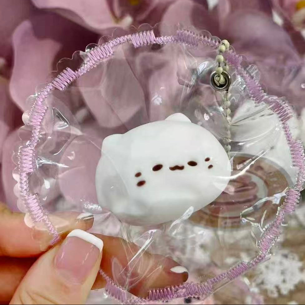 Handheld Mochi Meow Taba Squishy showing the cute white mochi cat face and detailed frilled packaging, handmade by Pawkemon.
