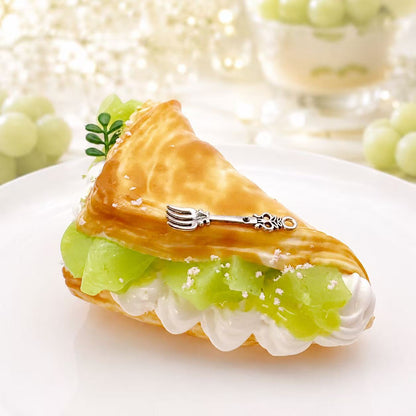 Close-up view of the Muscat Delight Taba Squishy, highlighting the glossy muscat grape filling, white cream details, golden pastry texture, leafy accent, and silver fork charm.