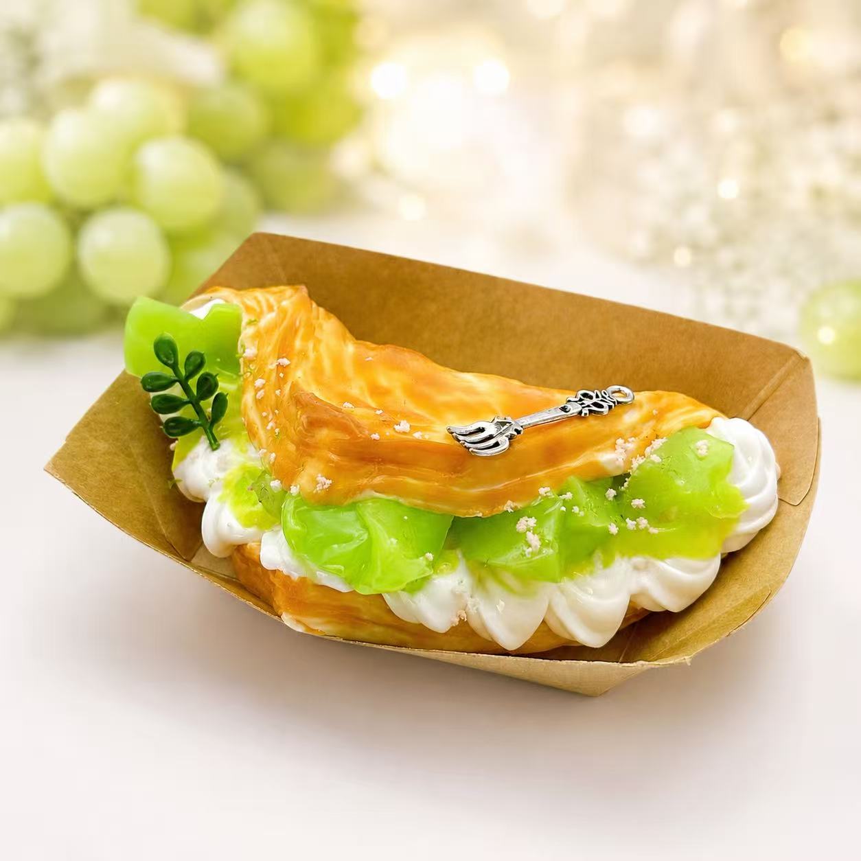 Muscat Crepe Taba Squishy by Pawkemon Squishy, a handmade silicone dessert squishy with green muscat grapes, cream layers, golden pastry topping, and tiny fork charm.