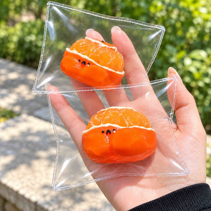 Two orange hamster Taba squishies in separate clear pouches rest one above the other on an open hand outdoors, showing their palm-sized scale and glossy orange fruit details.