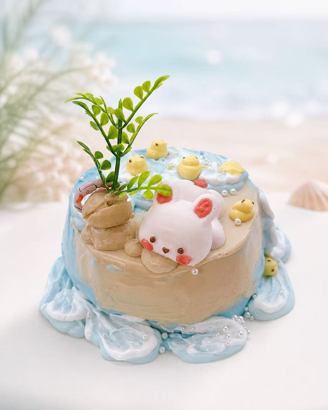 Handmade Bunny Beach Cake Taba Squishy with ocean wave icing, tiny yellow ducks, pearl details, and a sleeping bunny on a pastel beach cake.