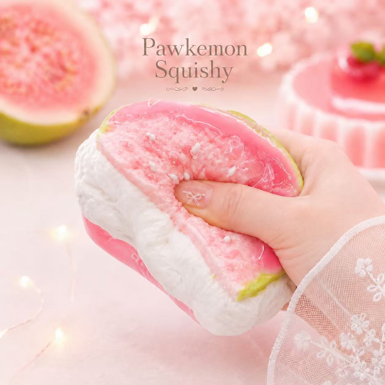 Guava squishy toy with a hand holding it, set against a soft pink background.
