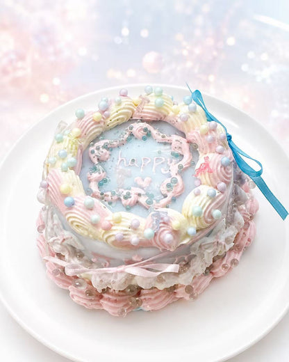Handmade Ocean Cake Taba Squishy with pastel blue center, “happy” lettering, pink and cream piping, pearl details, and a blue ribbon accent.