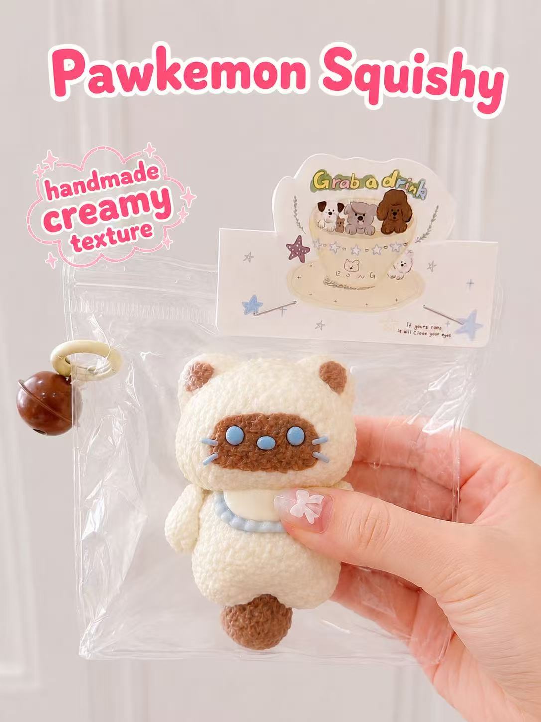 Hand holding the Siamese Cat Taba Squishy, showing its soft handmade silicone texture, slow-rising creamy feel, cute cat face, blue collar, and clear display packaging.