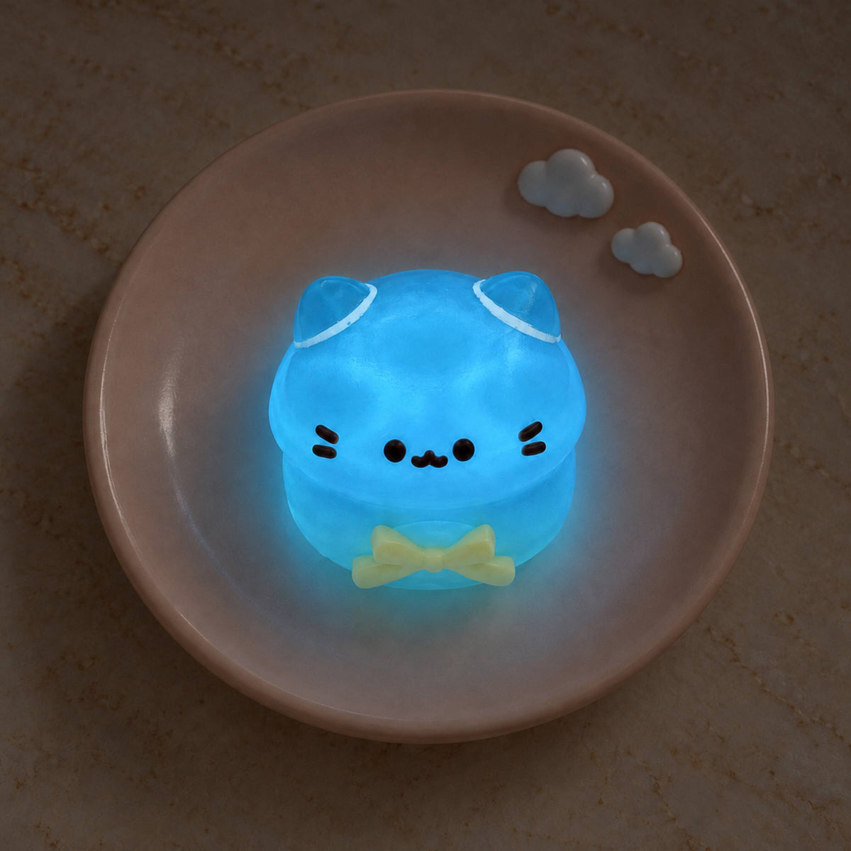 Translucent mini cat Taba Squishy glowing bright blue with black whiskers and a yellow bow on a pink plate.