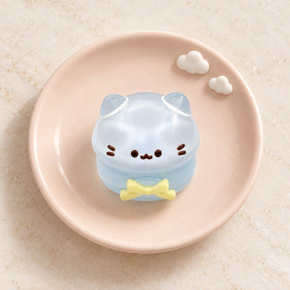 Clear pale-blue mini cat Taba Squishy with rounded ears, black whiskers and a yellow bow on a blush pink plate.