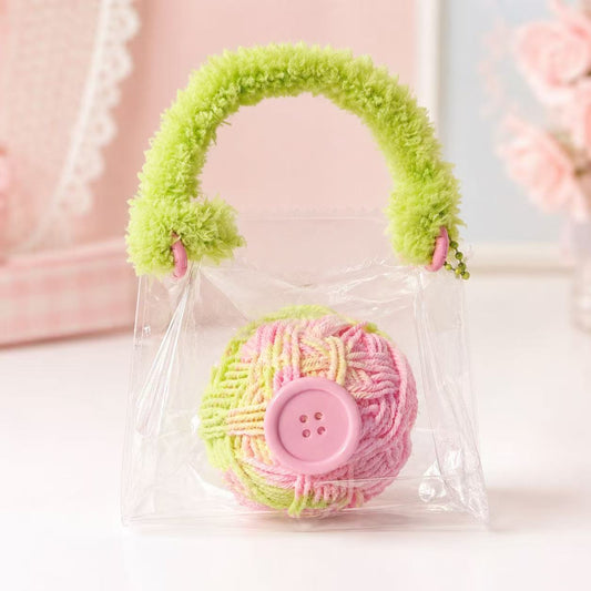 Yarn Ball Taba Squishy by Pawkemon Squishy, a handmade silicone squishy in clear purse packaging with a colorful yarn ball design, pink button detail, and fluffy green handle.